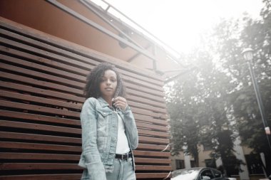 Siyah, genç ve güzel bir kız dışarıda dinleniyor. Sokak hipster portresi. Yürüyen öğrenci kadın.