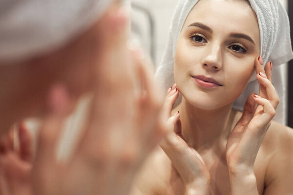 Young woman in bathroom behind mirror. Skincare  treatment concept