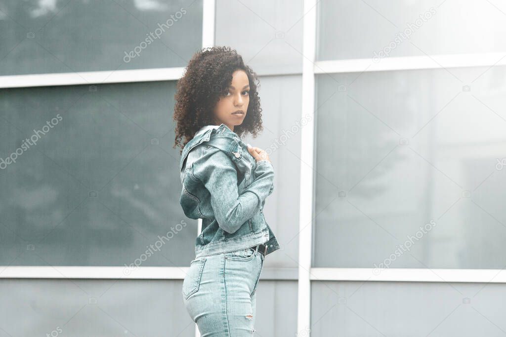 Mulatto black curly girl on street. Sunny summer city. Young woman denim style