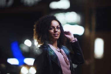Şehir caddesinde gece vakti şık bir kadın. Siyah kıvırcık saçlı güzel Afrikalı Amerikalı kadın.