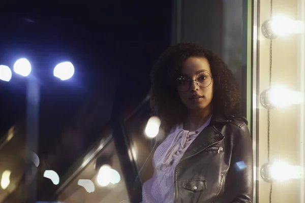 Fashionable woman on urban city street at night. Beautiful african american woman with black curly hair