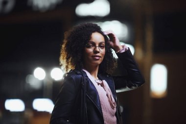 Şehir caddesinde gece vakti şık bir kadın. Siyah kıvırcık saçlı güzel Afrikalı Amerikalı kadın.