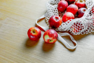 Ahşap masa üstünde yeniden kullanılabilir ağ torbasında taze kırmızı elmalar..