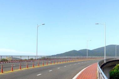 Açık bir günde sokak lambaları ve dağ arkaplanı olan boş kıvrımlı otoyol.