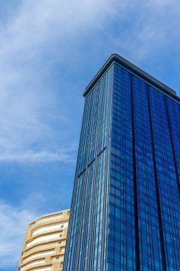 Tall glass skyscraper against blue sky with adjacent beige building.