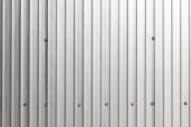 Corrugated metal wall with fasteners in industrial setting.