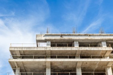 Concrete building under construction against blue sky with steel bar details.