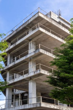 Concrete building under construction with metal rails and blue sky.