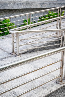 Stainless steel handrails with greenery on concrete steps in outdoor urban setting.