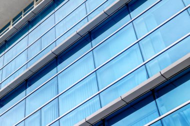 Modern glass building facade with blue windows reflecting sky.