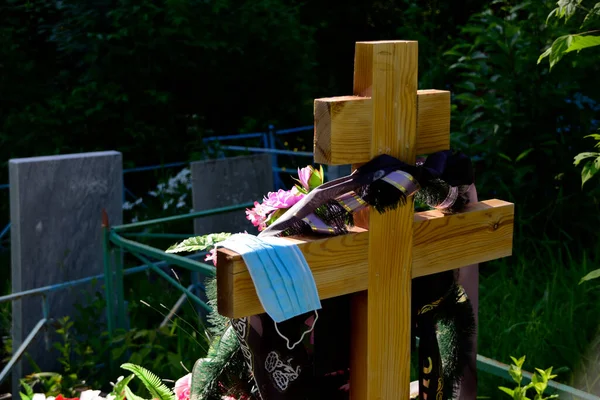 Fresh grave in the cemetery. On a simple wooden cross lies a disposable medical mask. Total quarantine from coronavirus in the Perm region.