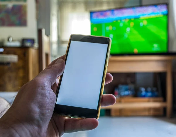 电视上的足球比赛中 男性手特写使用了白色屏幕的智能手机 — 图库照片