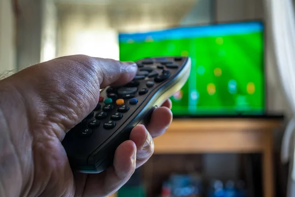 closeup of male hand uses the remote control during a football game on TV