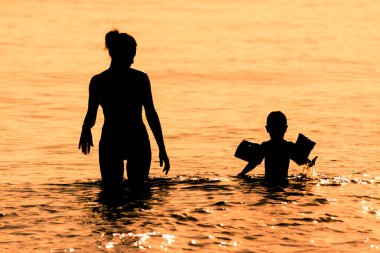 Gün batımında denizde şişme kol dayama, anne ve oğlu, ikinci silüeti giyer