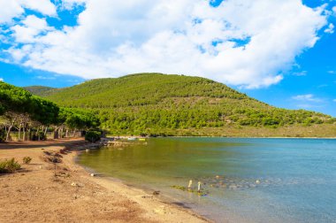 Capocaccia sahilinde, güneşli ve bulutlu bir günde Tramariglio körfezi, iskele ve plaj manzarası