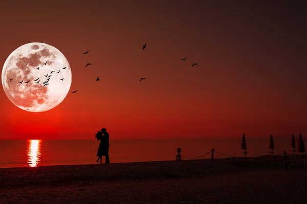 Silueta de una pareja besándose bajo luna llena al atardecer Imágenes de stock libres de derechos