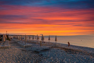 Sahilde sıra sıra kapalı şemsiyeler dramatik renkli gündoğumunda