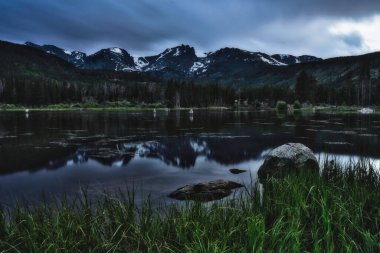 Sunset on Sprague lake in the rocky mountains of colorado. People fly fishing under the shadow of the beautiful mountain range clipart