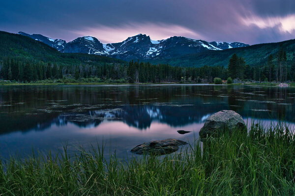 Sprague lake in colorado. Long exposure sunset in rocky mountain national park. Colorado rockies mountain visible in the distance. Colorful sunset with fiery clouds