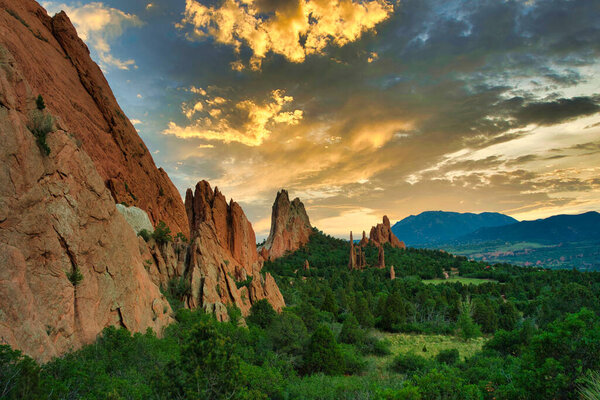 Garden of the Gods with colorful sunset. Beautiful colors cast light on the rock formations in colorado springs. Colorful clouds, green trees, and orange rocks visible