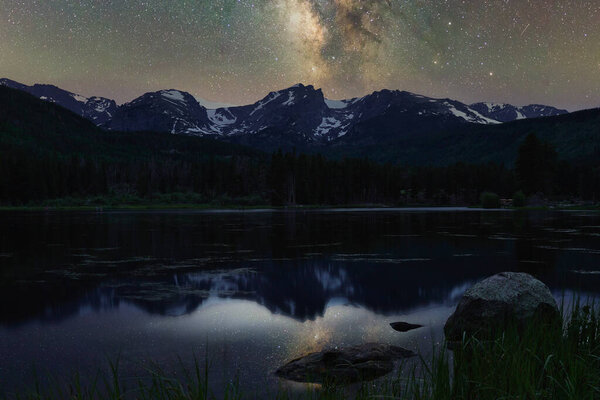 Milky Way reflecting off water around rocky mountain national park. Sprague lake at night reflects stars on glassy smooth water. Long exposure