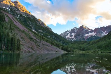 Maroon Bells 'deki Hillside. Göl, günbatımındaki tepeleri yansıtır. Güzel altın saat gökyüzü, su yansımaları ve görünen renkli zirveler.