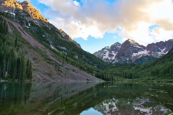 Maroon Bells 'deki Hillside. Göl, günbatımındaki tepeleri yansıtır. Güzel altın saat gökyüzü, su yansımaları ve görünen renkli zirveler.