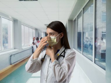 Healthcare worker in white coat putting on mask in hallway before entering patient room. PPE demonstration in hospital setting clipart