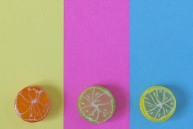 Narenciye (portakal, limon, limon) şeklinde renkli şeker yaratıcı görünümü yaz renkler renkli kağıt arka plan üzerinde. Kavramsal görüntü yazın. Minimalizm. Soyutlama. Yaratıcılık. Üstten görünüm.