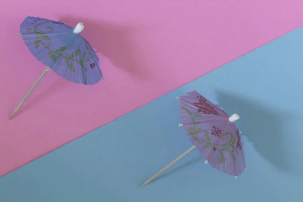 Creative view of a cocktail umbrella on a two-tone background - pink and blue. Conceptual image of summer. Minimalism.  Summertime. Top view.