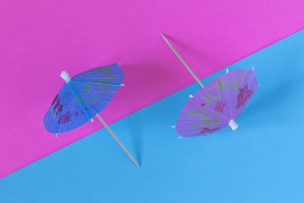 Creative view of a cocktail umbrella on a two-tone background - pink and blue. Conceptual image of summer. Minimalism. Abstraction. Summertime. Top view.