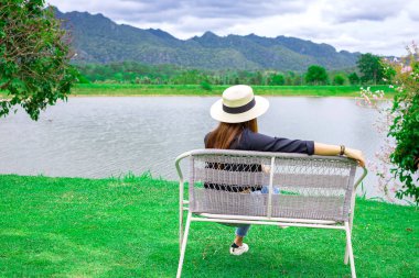 Göl kenarında dağ manzaralı bir bankta oturan kadın. Tatil zamanı kavramı.