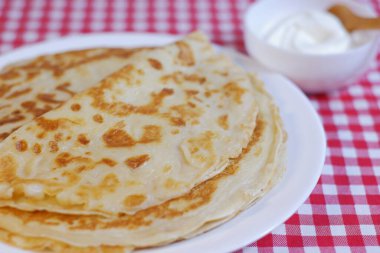 Lezzetli gözleme Rus mutfağı tabakta ve tatlı ekşi krema ile bir kaşık natürmort.