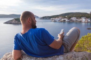 Gün batımında cep telefonuyla Mallorca 'daki Sant Elm sahil koyunda bir adam.