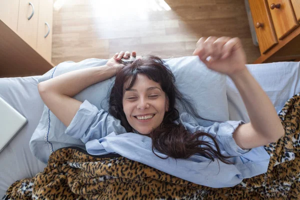 A young woman just woke up from a nap and using her mobile phone. Aerial view of woman lying in bed with matching leopard sheets and mobile. Just awakened.