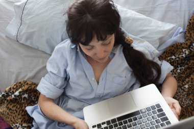 Yatakta yatan genç bir kadın, uykusundan yeni kalkmış ve dizüstü bilgisayarı yataktaydı. Kendine dikkat et..