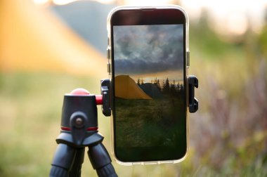 Bir tripodun üzerindeki akıllı telefon, sabahları dağlarda güneşin doğuşunun videosunu çeker. Dağlarda cep telefonu. Yalnız kamp. Cep telefonuyla dağlarda video yakalamak.