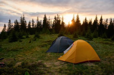 Sabahın köründe tepede iki çadır. Tepeye kurulmuş iki çadır, sabah güneşinin yumuşak ve renkli ışığında yıkanmış. Sabahleyin tepede kamp çadırı.