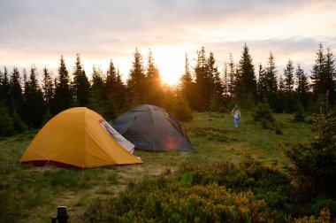 Sabahın köründe tepede iki çadır. Tepeye kurulmuş iki çadır, sabah güneşinin yumuşak ve renkli ışığında yıkanmış. Sabahleyin tepede kamp çadırı.