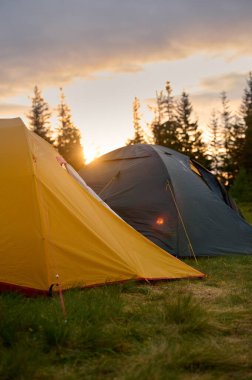 Sabahın köründe tepede iki çadır. Tepeye kurulmuş iki çadır, sabah güneşinin yumuşak ve renkli ışığında yıkanmış. Sabahleyin tepede kamp çadırı.