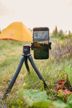 Bir tripodun üzerindeki akıllı telefon, sabahları dağlarda güneşin doğuşunun videosunu çeker. Dağlarda cep telefonu. Yalnız kamp. Cep telefonuyla dağlarda video yakalamak.