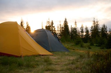 Sabahın köründe tepede iki çadır. Tepeye kurulmuş iki çadır, sabah güneşinin yumuşak ve renkli ışığında yıkanmış. Sabahleyin tepede kamp çadırı.