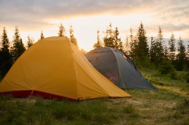 Sabahın köründe tepede iki çadır. Tepeye kurulmuş iki çadır, sabah güneşinin yumuşak ve renkli ışığında yıkanmış. Sabahleyin tepede kamp çadırı.