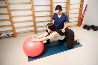 Hamile kadın, fitness topu kullanarak fizyoterapistle doğum öncesi egzersizleri yapıyor. Hamile müşteriye hamilelik fizyoterapi seansında rehberlik eden kadın uzman..