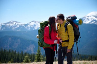 İki yürüyüşçü bir dağ sırtında mola veriyor. Sırt çantalı sportif çift, karlı dağların arka planında duruyorlar..