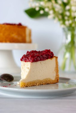 Ahududu soslu bir dilim peynirli kek beyaz bir masada duruyor..