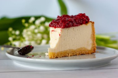 Ahududu soslu bir dilim peynirli kek beyaz bir masada duruyor..