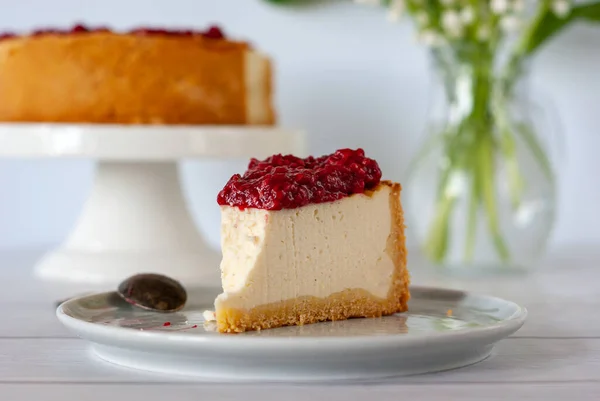 Ahududu soslu bir dilim peynirli kek beyaz bir masada duruyor..