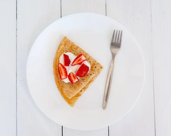 Tahta bir masada beyaz bir tabakta çilekli krepler. Üst görünüm