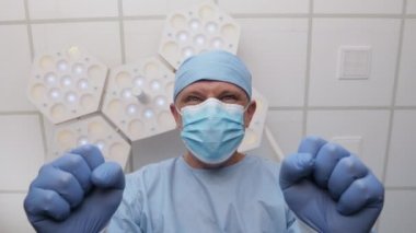 Lastik eldivenli kızgın doktor ameliyathanede hastanın başında dikiliyor.